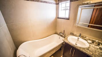 A bathroom with a freestanding bathtub, a sink with a granite countertop, and a mirror above the sink.