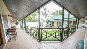 A covered outdoor area with a tiled floor, benches, and a view of a building with a green roof. - AnnVilla Guesthouse (Klerksdorp)