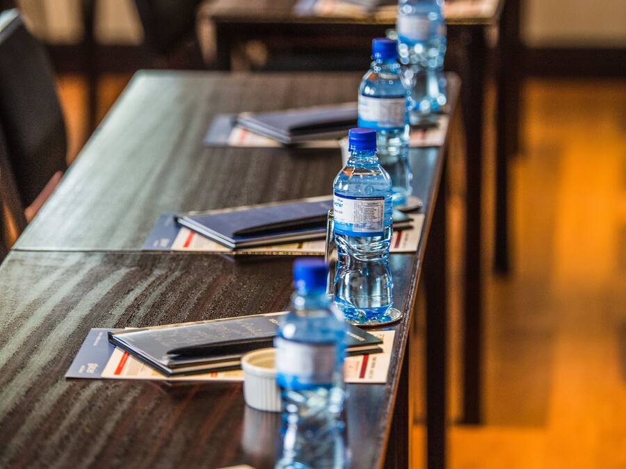 Un salón de conferencias con una larga mesa, botellas de agua y cuadernos.