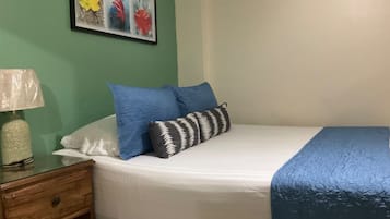 A neatly made bed with blue and white bedding, a wooden nightstand with a lamp, and a framed artwork on the wall.