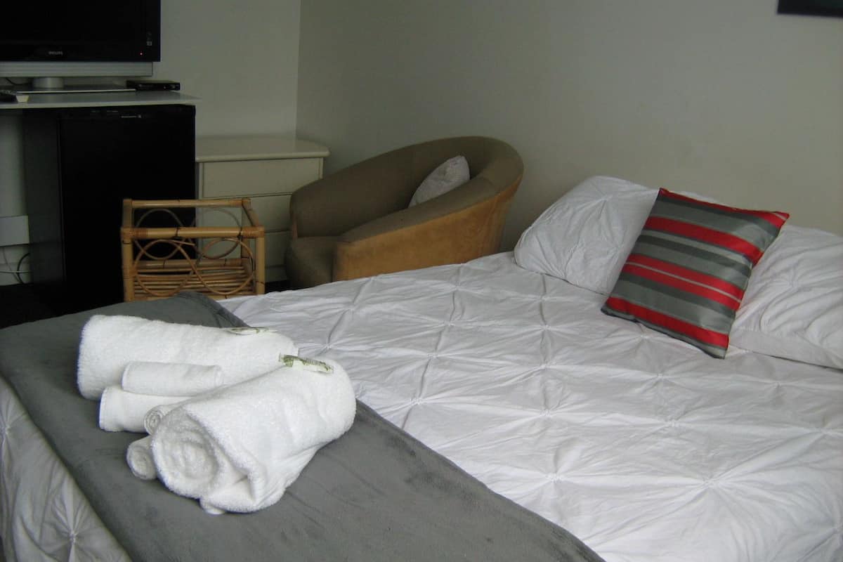 A neatly made bed with white and gray bedding, a striped pillow, and rolled towels on the side.