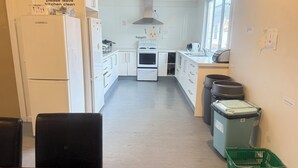 A compact kitchen with white appliances, a dining table, and trash bins. - Downtown Backpackers (Nelson)