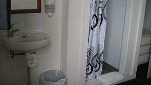 A bathroom with a sink, a hand soap dispenser, a shower curtain, a trash bin, and a towel rack. - Downtown Backpackers (Nelson)