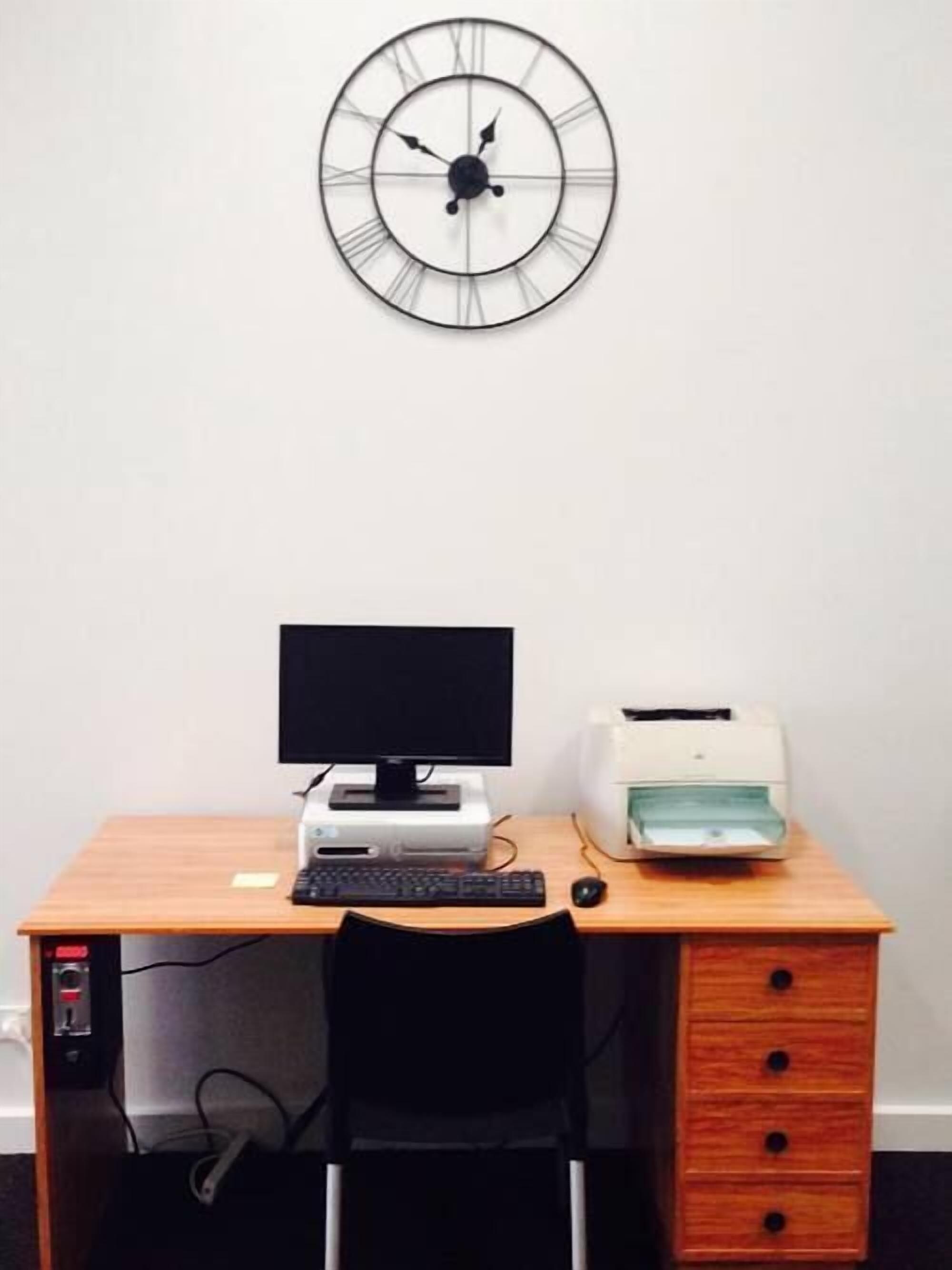 Un escritorio de madera con un monitor de computadora, teclado, ratón e impresora.