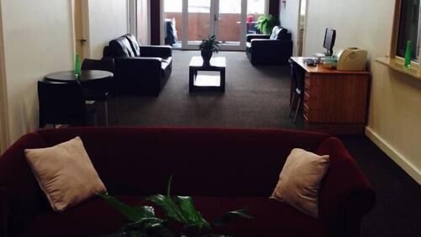 A lobby with a red sofa, black armchairs, a coffee table, and a desk with a computer. - Downtown Backpackers (Nelson)