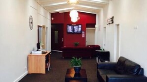 A spacious lobby with a high ceiling, a reception desk, a seating area with a sofa and armchair, and a potted plant. - Downtown Backpackers (Nelson)