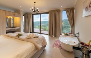 A spacious bedroom with a large bed, a bathtub, and a balcony with a scenic view.
