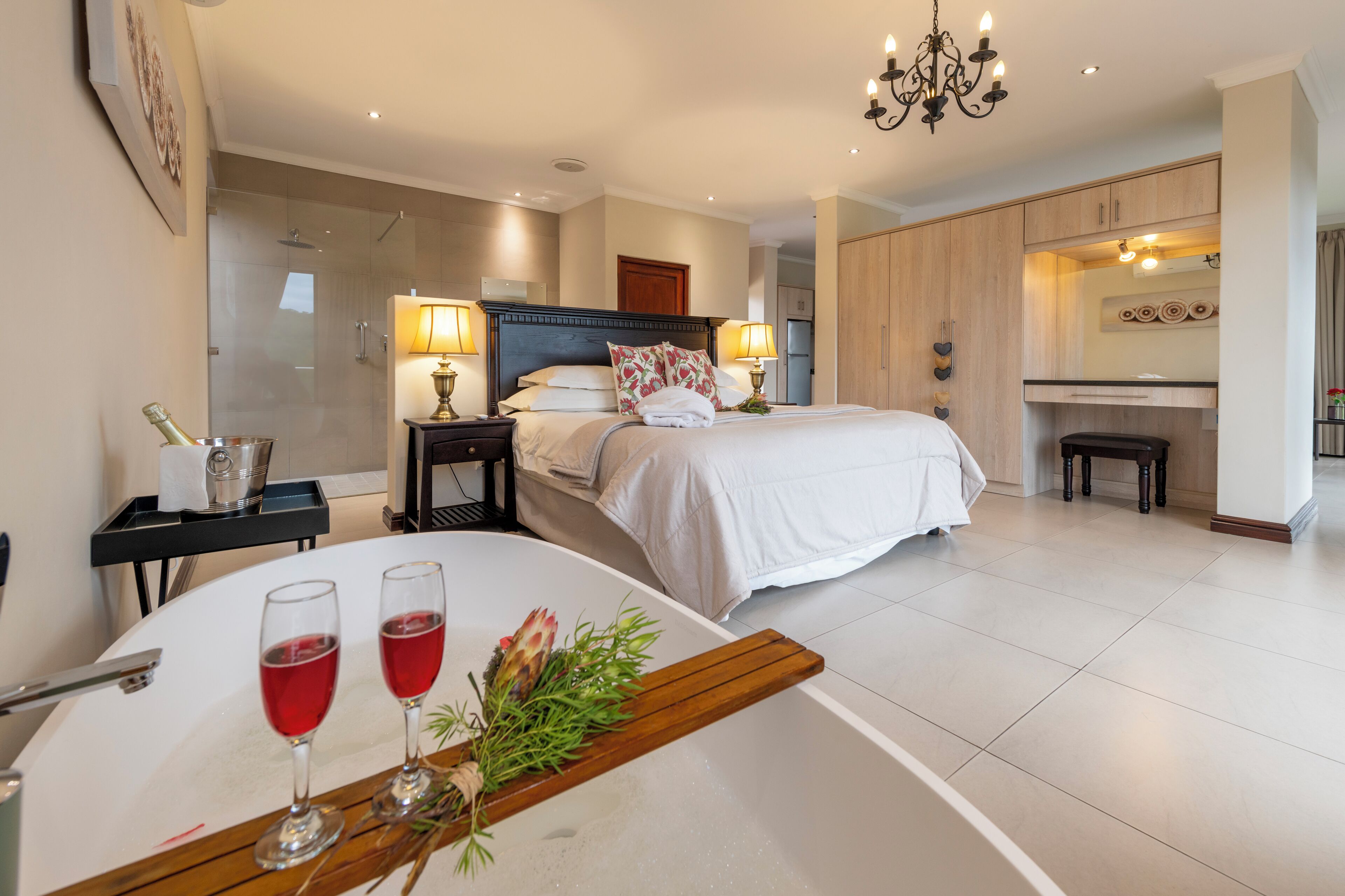 A modern hotel room with a large bed, bedside lamps, a bathroom, and a dining area with a table set for two.