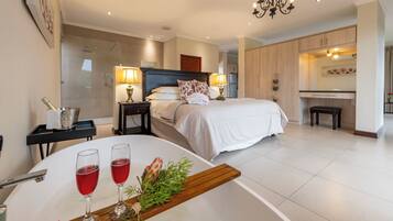 A modern hotel room with a large bed, bedside lamps, a bathroom, and a dining area with a table set for two.