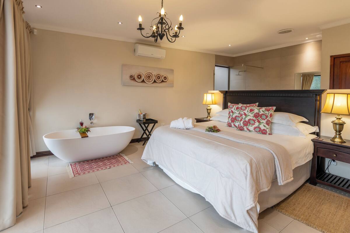 A modern bedroom with a large bed, a freestanding bathtub, and a chandelier.