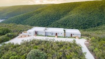 Un bâtiment moderne à plusieurs étages, doté d’un toit plat, entouré d’une forêt verdoyante et de collines.