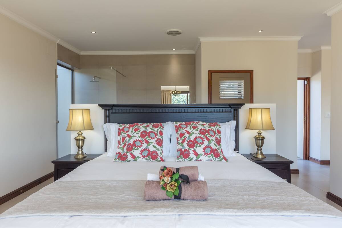 A hotel room with a large bed, two bedside tables with lamps, floral-patterned headboards, and a view of the hallway.