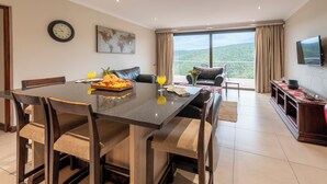 A dining area with a table set for four, a sofa, and a TV mounted on the wall. - Alkantmooi Nature Reserve Keurkloof Units (Plettenberg Bay)