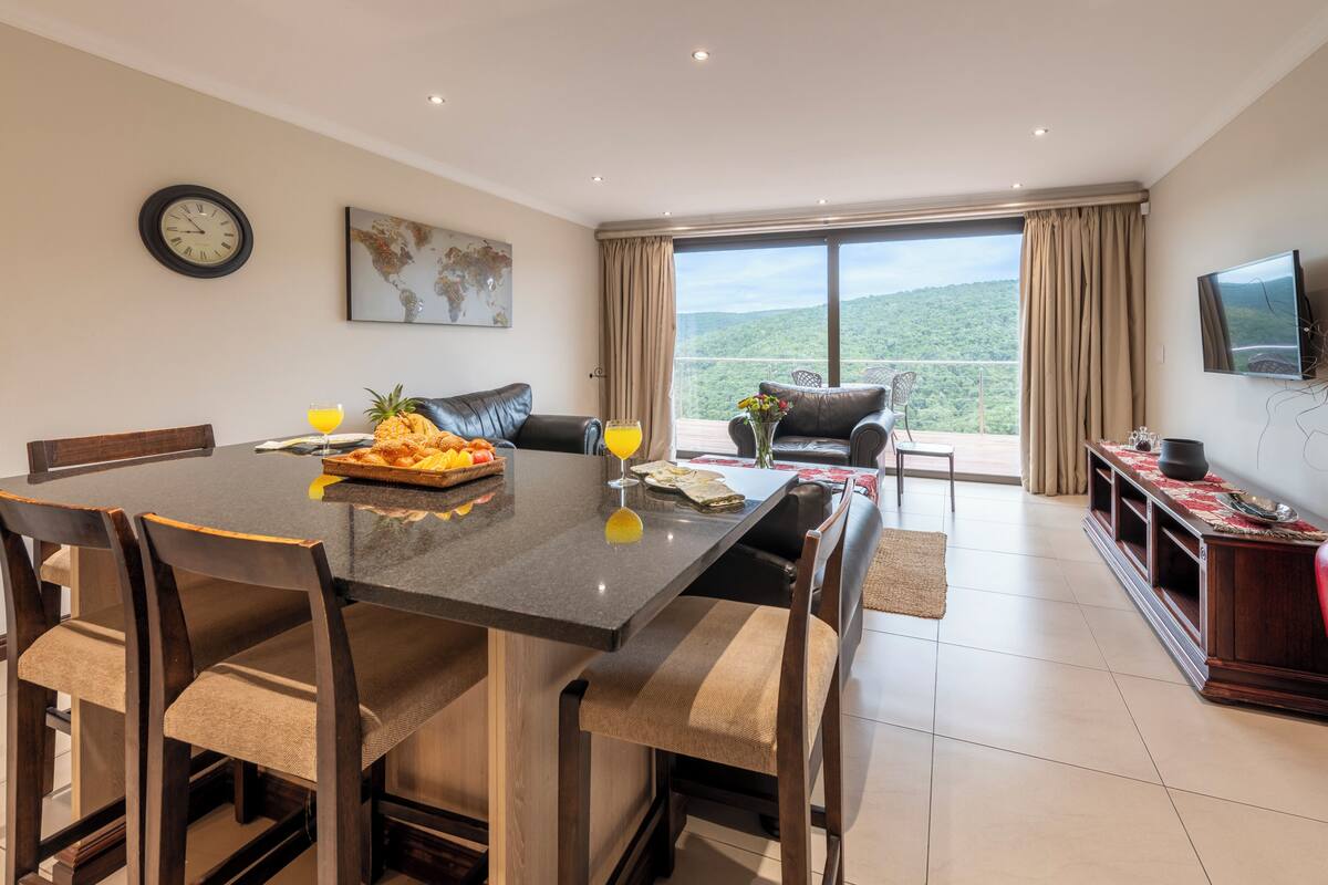 A dining area with a table set for four, a sofa, and a TV mounted on the wall.