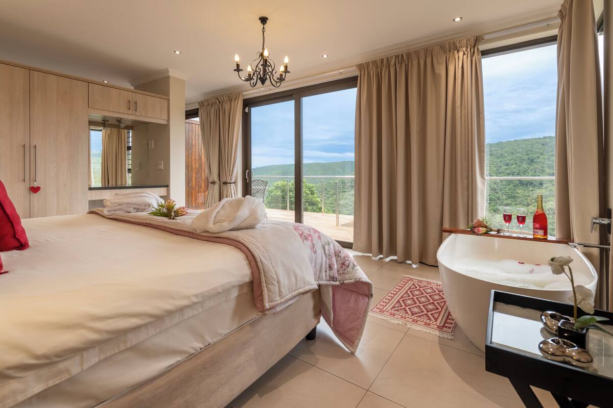 A bedroom with a large bed, a bathroom with a bathtub, and a view of the outdoors.