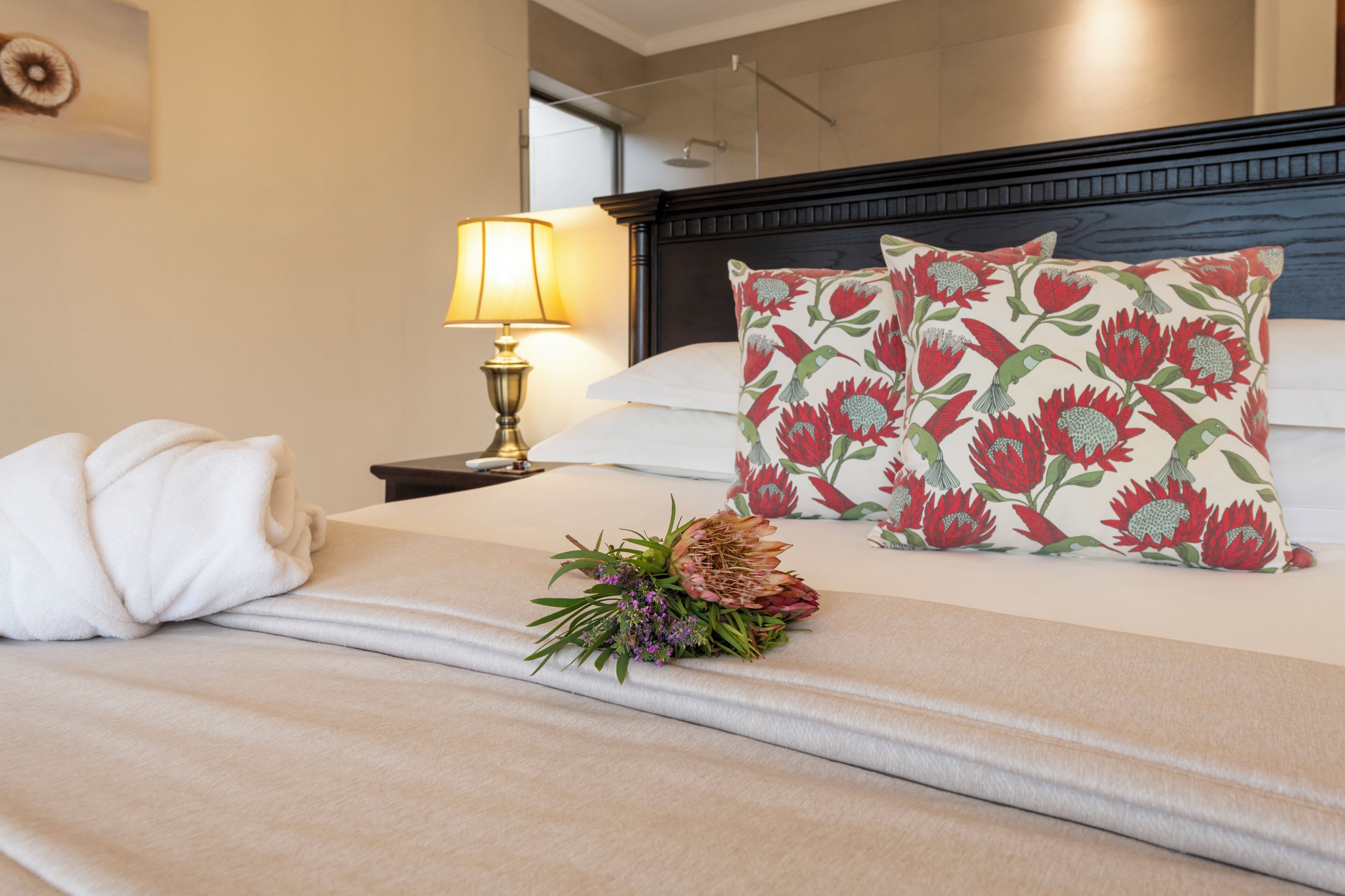A neatly made bed with floral pillows, a bedside lamp, and a decorative flower arrangement.