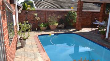 Relax by the rectangular pool surrounded by lush greenery and a brick wall.