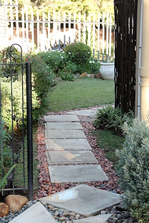 Un sentier de jardin bordé de pierres plates, une clôture blanche et diverses plantes.