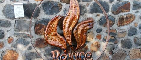 Un muro de piedra con un letrero de metal que muestra pescado a la parrilla y la palabra "Rejoice".