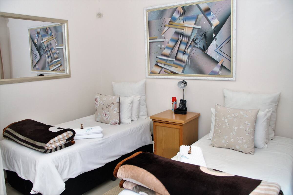 Habitación de hotel con dos camas, una mesita de noche y obras de arte en las paredes.