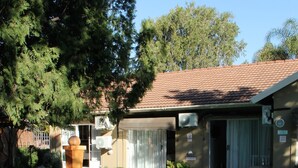 A swimming pool with white chairs, a patio area, and a building with a tiled roof. - Memra Guest House (Ladysmith)