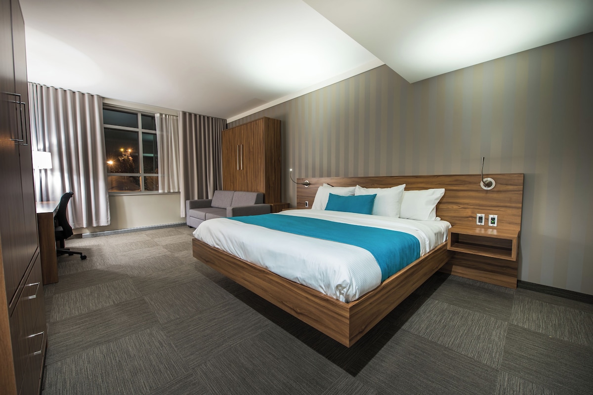 A modern hotel room with a large bed, a desk, and a wardrobe.
