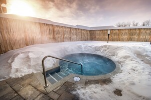 Un jacuzzi rodeado de nieve, con una valla de madera al fondo.