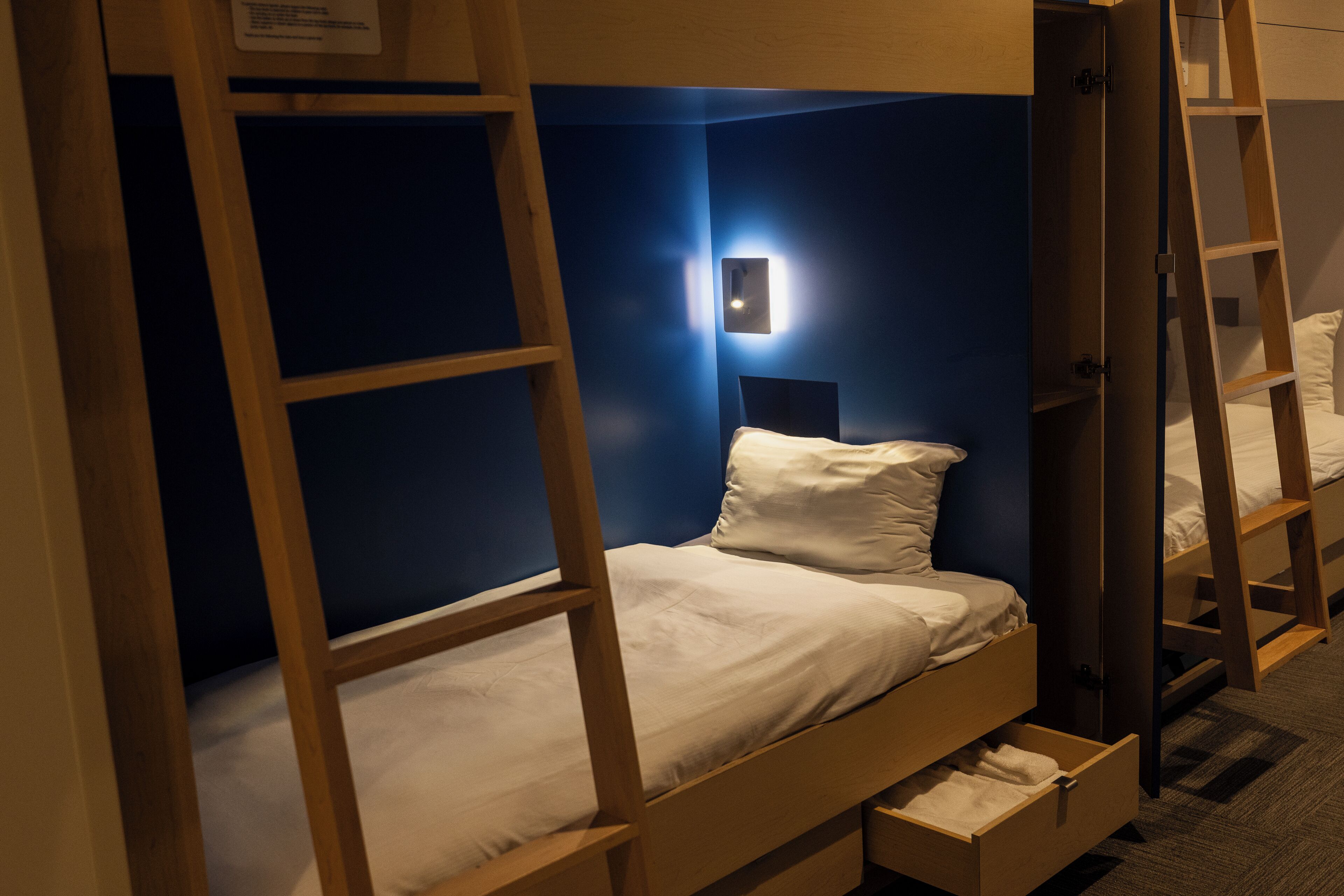 Un lit superposé avec une échelle en bois, une table de chevet et une lampe fixée au mur.