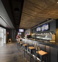 Zona de bar con una barra larga, varios taburetes y una pantalla de televisión sobre la barra.