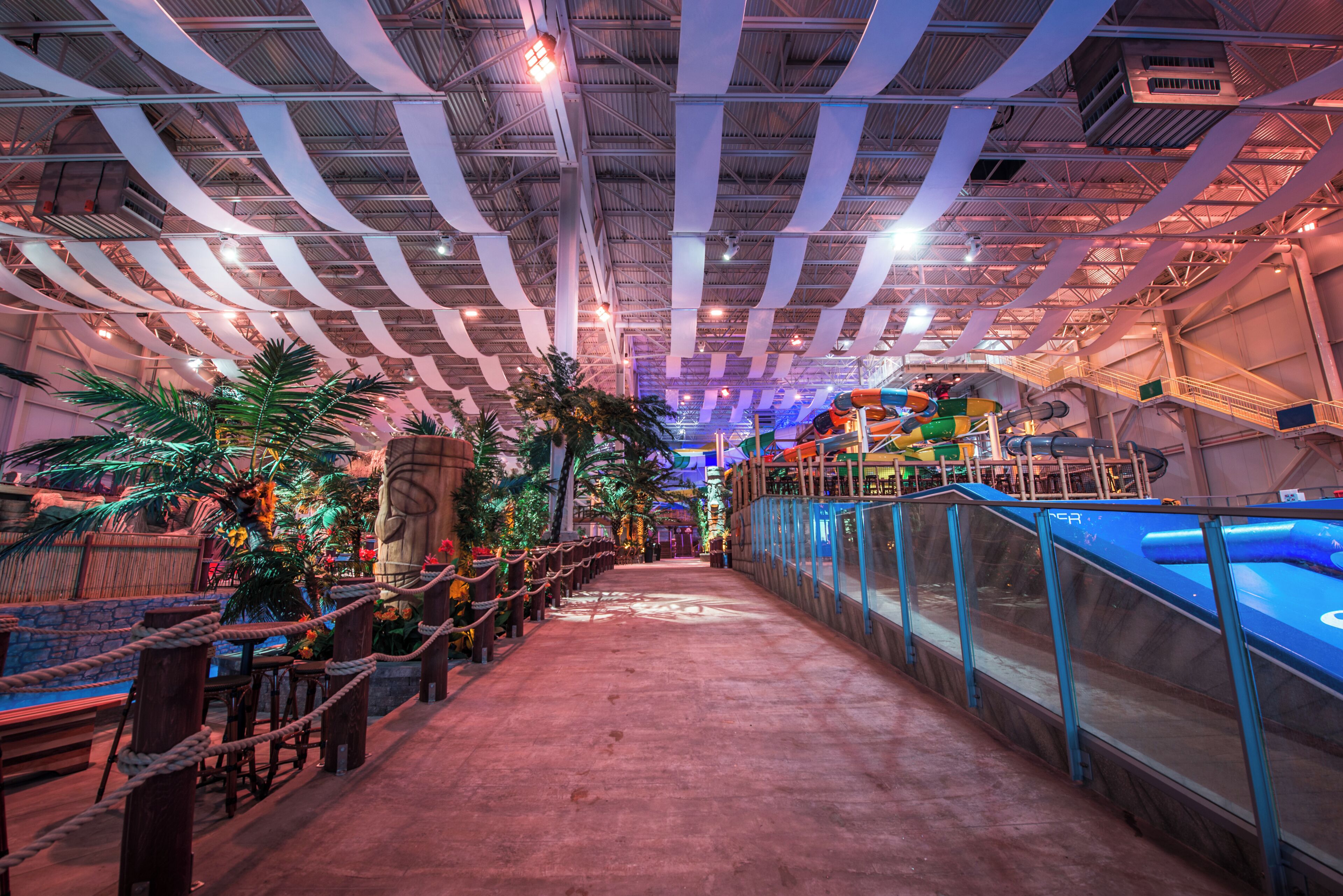 Un espacio interior con techos altos, iluminación de estilo industrial, y un camino central flanqueado por zonas de estar y una fuente de agua.