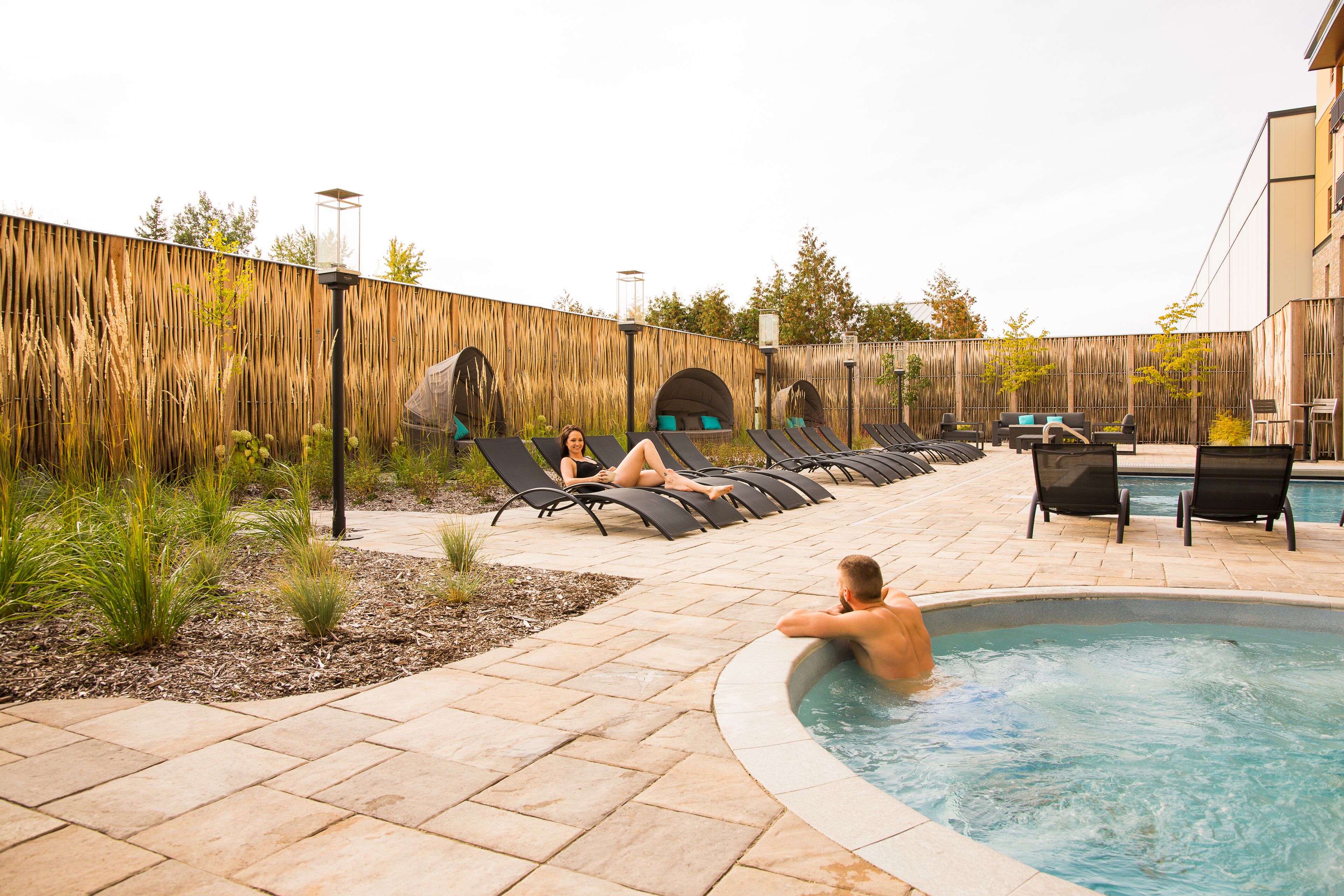 A pool area with lounge chairs, a hot tub, and a wooden fence.