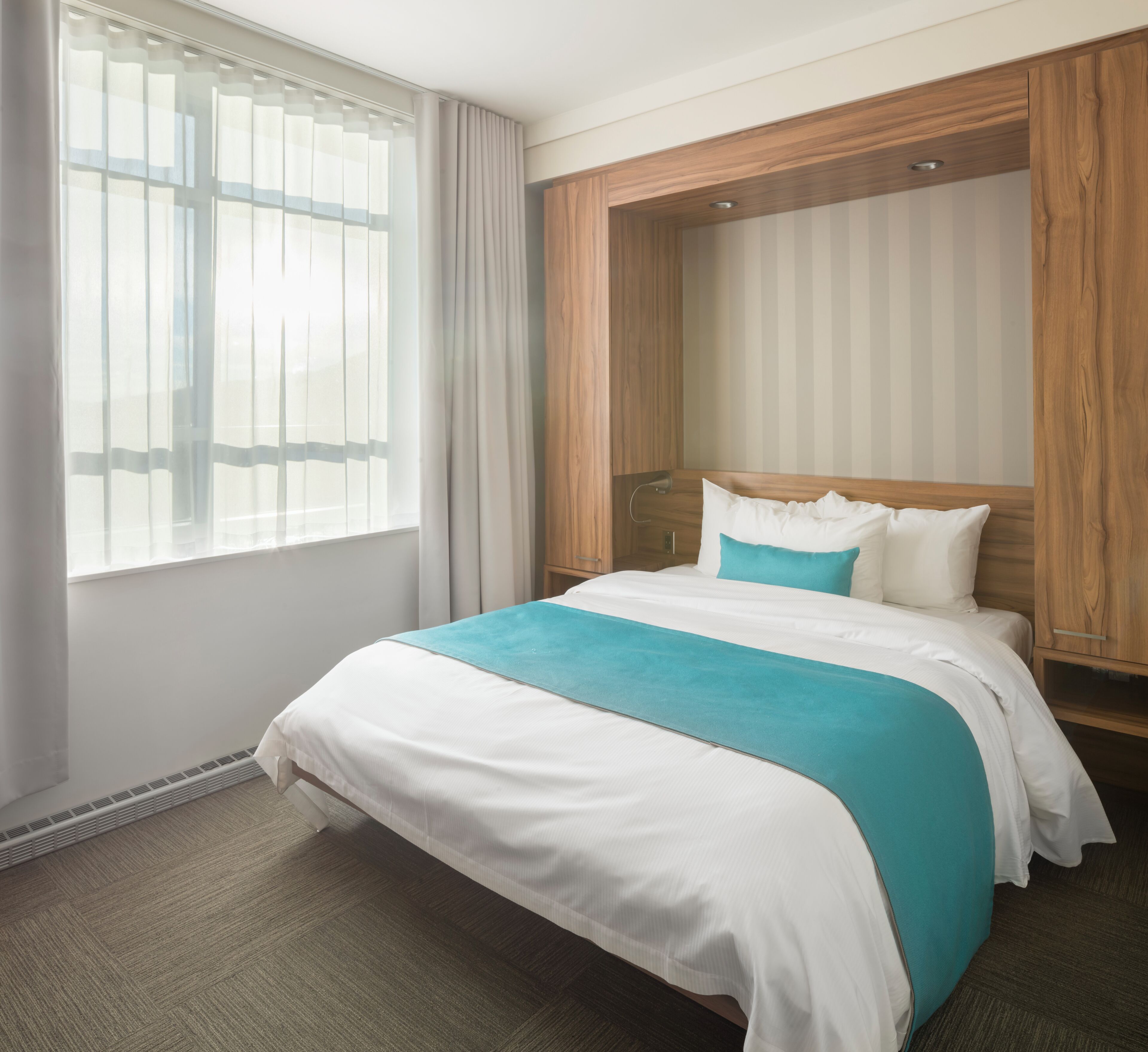 Een hotelkamer met een bed, een houten hoofdbord, een raam met gordijnen en een radiator.