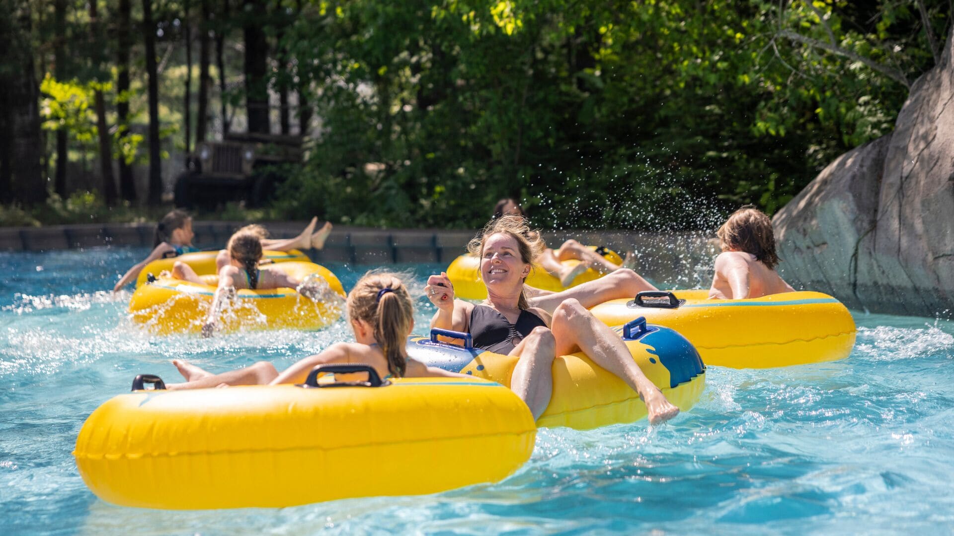 Menschen treiben auf gelben Luftmatratzen in einem von Bäumen umgebenen Pool.