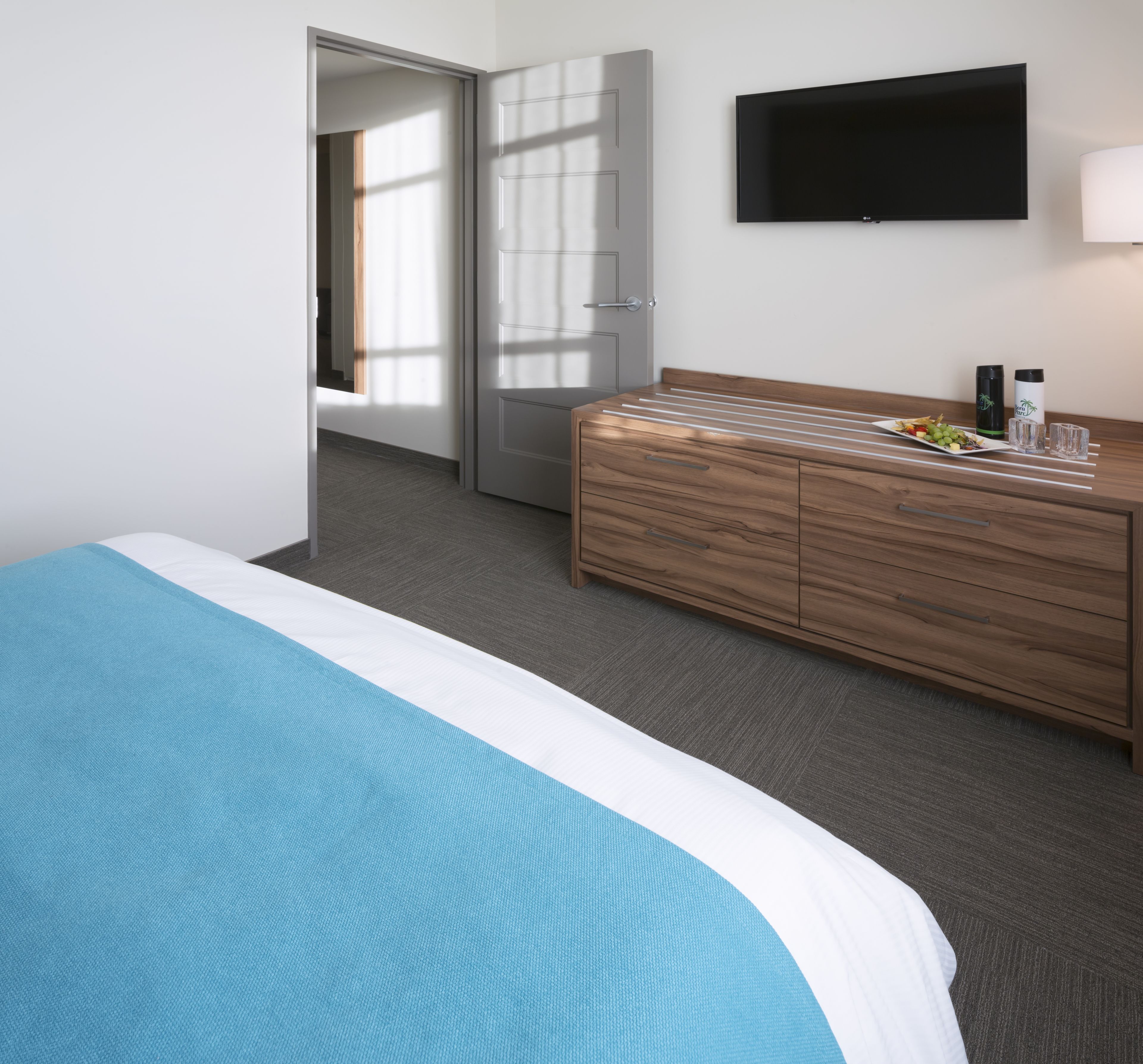 Ein Hotelzimmer mit einem Bett, einem Holzschrank, einem Flachbildfernseher und einem kleinen Tisch mit Obstplatte und Gläsern.