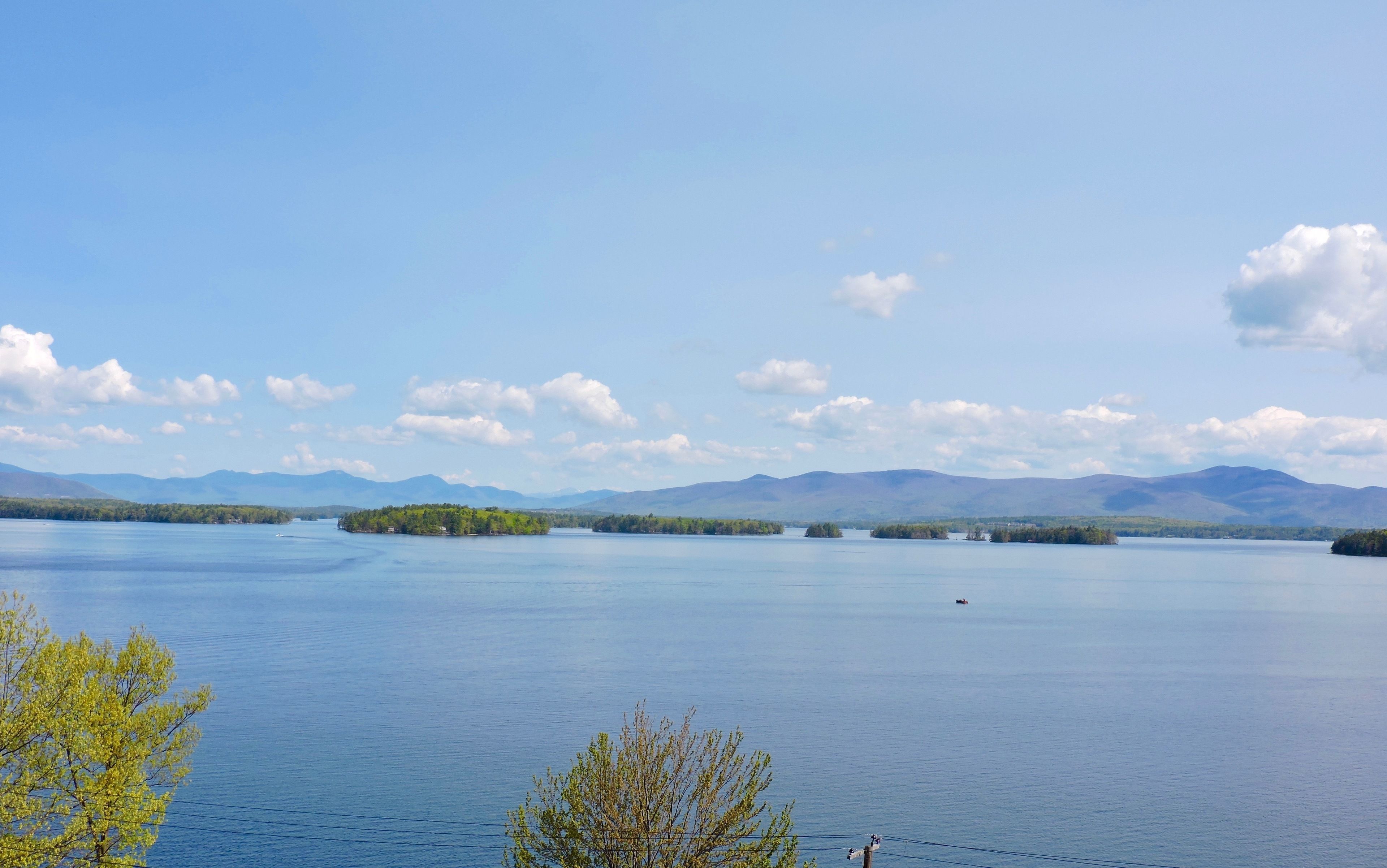 Una extensa masa de agua con varias islas pequeñas, cielo despejado y montañas a lo lejos.