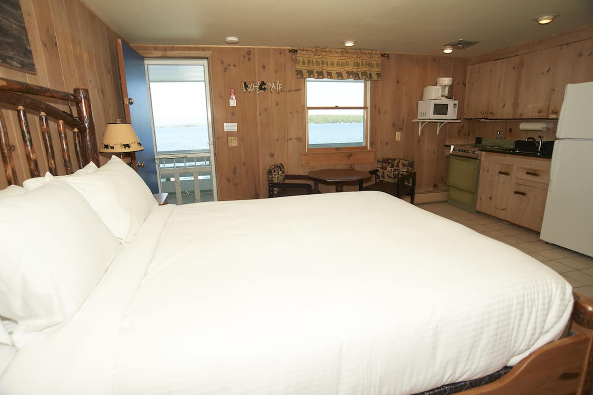 A bedroom with a large bed, a small table, a chair, a microwave, and a refrigerator.