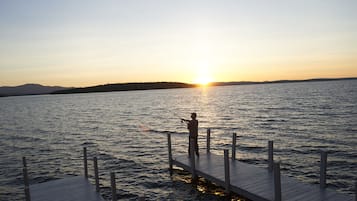 A person fishing at a wooden dock extending into a body of water during sunset.