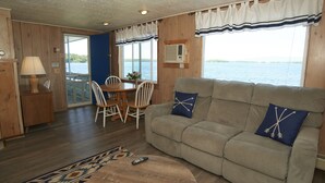 A cozy cabin interior with a sofa, dining table, chairs, and a remote control on a round table. - Belknap Point Inn (Gilford)