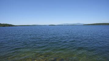 Ein ruhiger See mit klarem Wasser, umgeben von bewaldetem Land und fernen Bergen.
