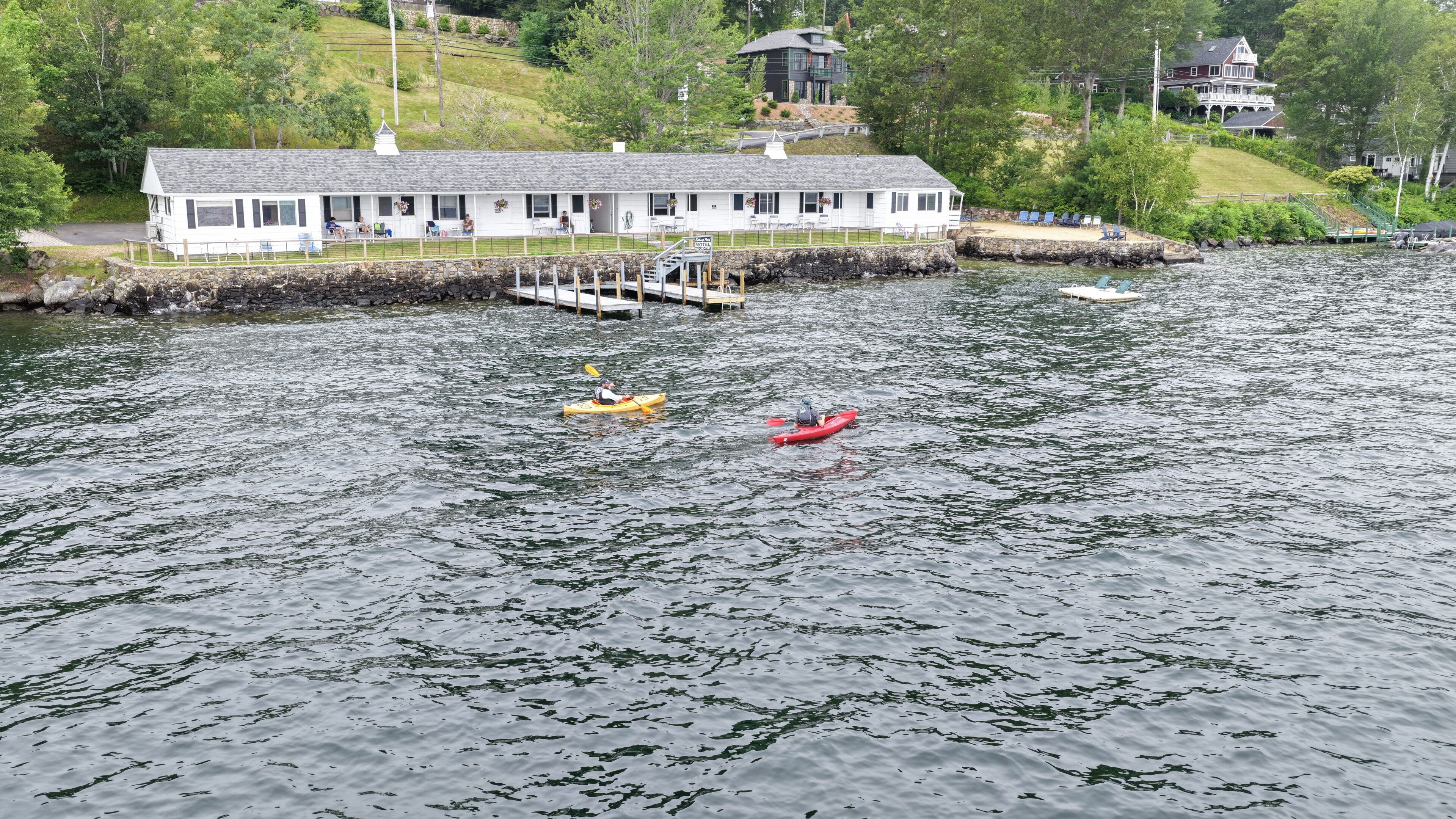 Un lodge sul lago con un molo, kayak e un edificio bianco con veranda.