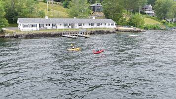 A lakeside lodge with a dock, kayaks, and a white building with a porch.