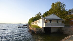 A waterfront building with a stone dock extending into the water, a grassy area, and a clear sky. - Belknap Point Inn (Gilford)