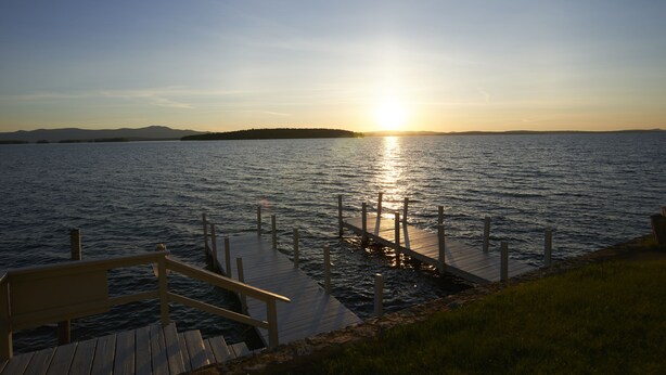 A wooden pier extending into calm water with a sunset in the background. - Belknap Point Inn (Gilford)