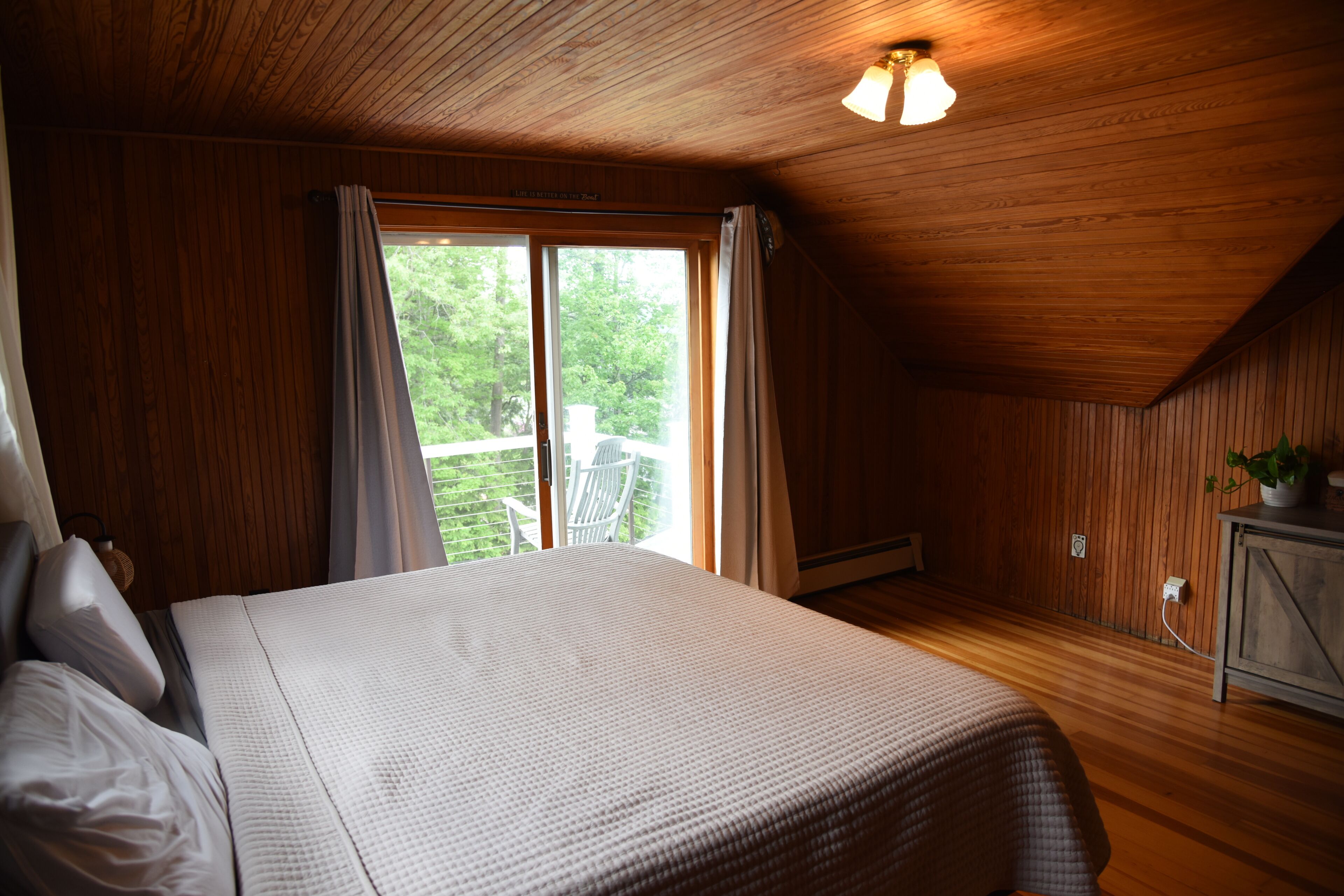 Ein Schlafzimmer mit einem großen Bett, Holzwänden, einer Deckenleuchte und einem Fenster mit Vorhängen.