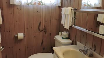 Un baño con paredes de madera, un inodoro, un lavabo y una cortina de ducha con motivos florales.