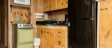 Une cuisine de taille réduite, avec des meubles en bois, un réfrigérateur noir, une cuisinière verte et un four à micro-ondes.