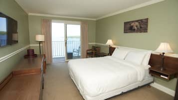 A hotel room with a large bed, two bedside tables with lamps, a desk, a chair, and a balcony with a view.