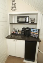 Una kitchenette compacta con microondas, cafetera y dispensador de cápsulas de café.
