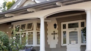 Et hus med en overdækket veranda, en hvid dør og en lille have med et træ og blomster.
