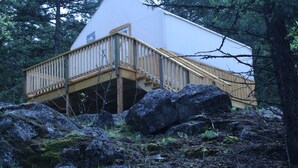 Una cabaña con terraza de madera y escaleras, rodeada de rocas y árboles.